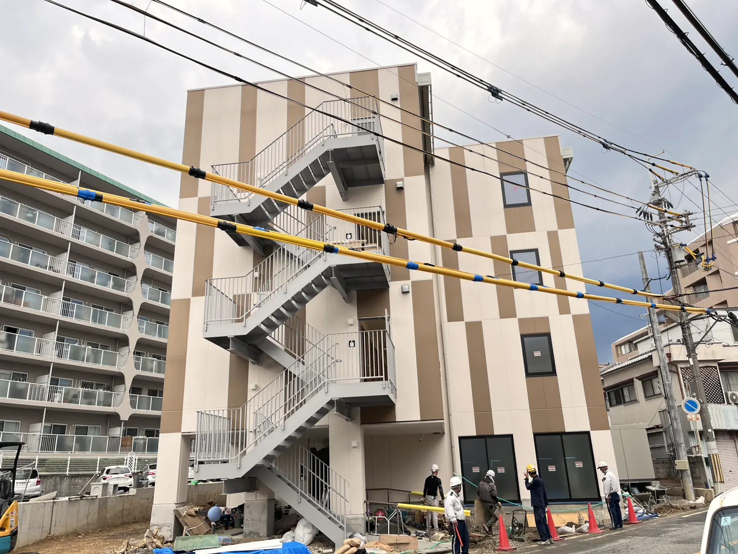 完成後の4階建て老人ホーム。ベージュ2色を縦に塗り分けた外壁と、グレーに塗り替えられた外階段